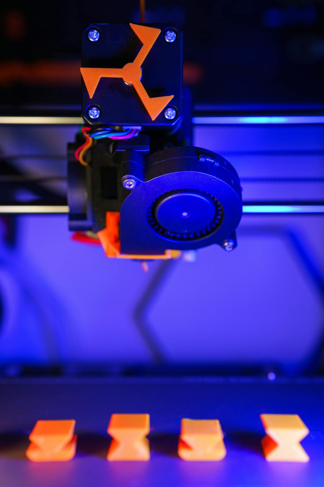 A 3D printer illuminated with neon lights crafting vibrant orange models.