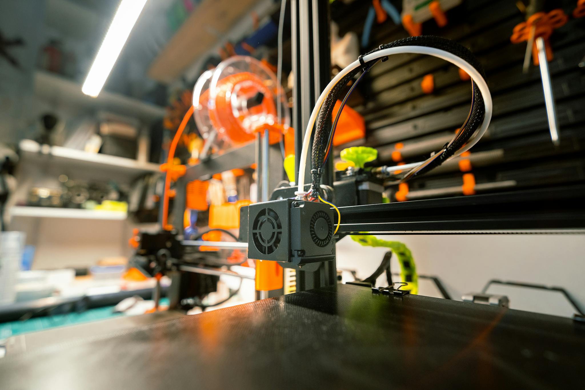 Close-up of a 3D printer in a workshop with visible tools and spool.