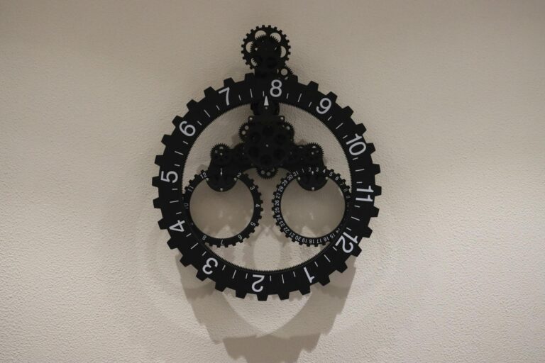 Close-up of a modern industrial gear wall clock on a plain wall, showcasing intricate design.