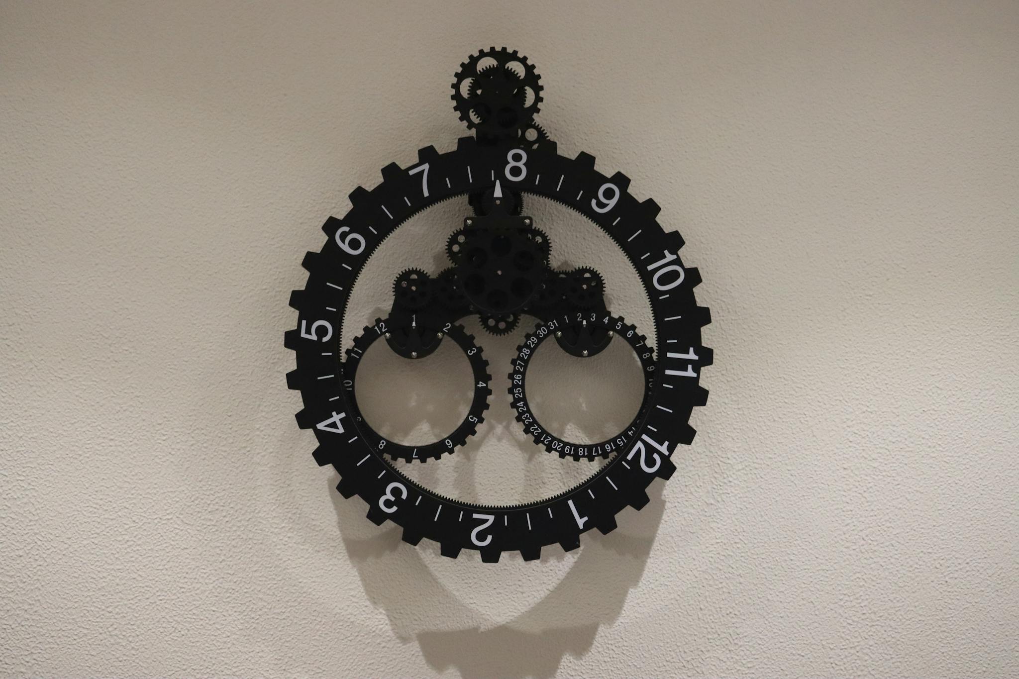 Close-up of a modern industrial gear wall clock on a plain wall, showcasing intricate design.