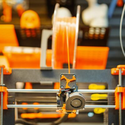 Close-up of an advanced 3D printer extruding filament in a workshop setting.